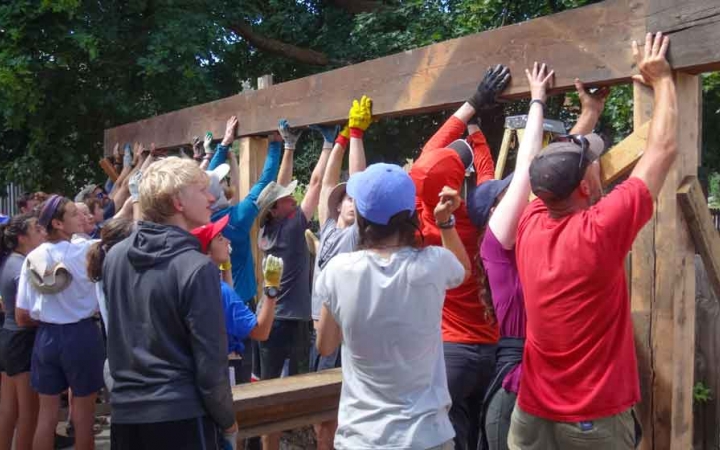 A group of people raise a long piece of wood during a service project. 